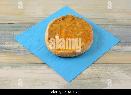 Orange marmalade on whole wheat English muffin half on blue napkin on table Stock Photo