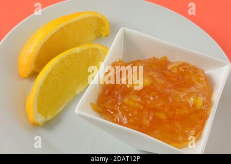 Orange marmalade jam preserves in white condiment bowl and orange slices on white plate on orange background Stock Photo