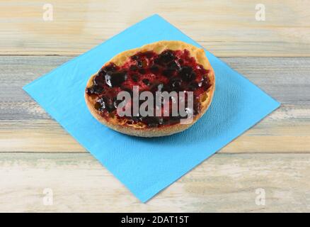 Whole wheat English muffin with black currant jelly preserves on blue napkin on table Stock Photo