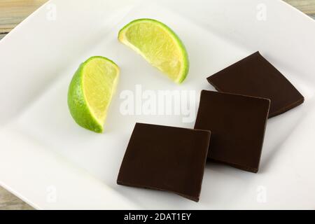 Lime and mint dark chocolate bar pieces with fresh lime wedges on white dessert plate Stock Photo