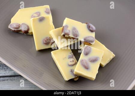 Almond white chocolate candy bar pieces with whole almond nuts on brown plate Stock Photo