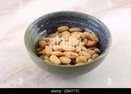 Whole almonds seasoned with Himalayan pink salt in ceramic snack bowl on table Stock Photo