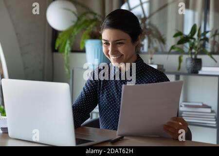 Smiling Indian businesswoman using laptop, checking financial documents Stock Photo