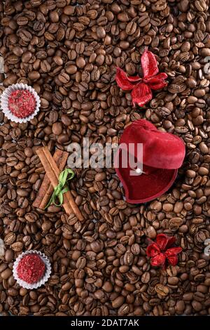 Coffee beans on a coffee beans background with red flowers , red chocolate and cinnamon. Morning espresso. Coffee mug. Stock Photo