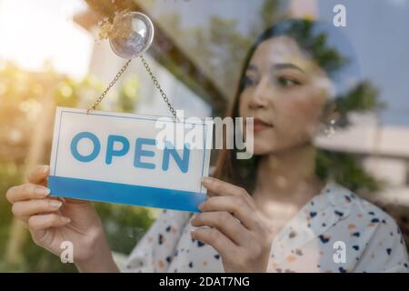 young woman owner turning open sign in door of store Stock Photo