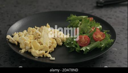 scrambled eggs on black plate with salad, wide photo Stock Photo
