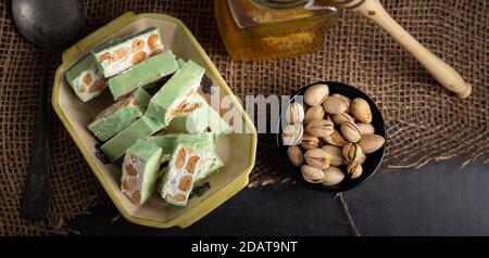 Organic nougat made with honey, pistachio, hazel nut, and almond nuts on a rustic dark background. Stock Photo