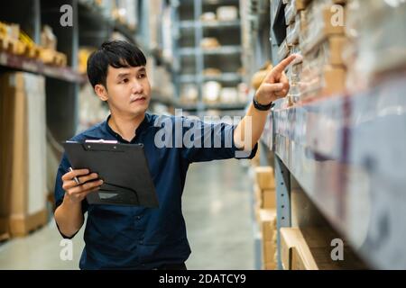 young man worker holding clipboard and checking inventory in the warehouse store Stock Photo