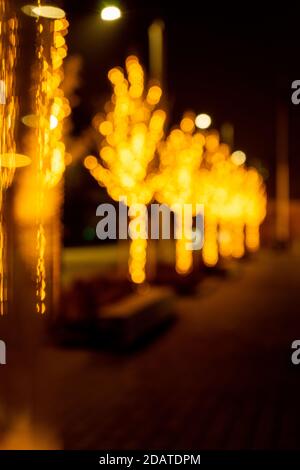 Cozy evening in the festive city. Blurred image of trees decorated with light garlands for Christmas and New Year celebration time. Shining trees Stock Photo