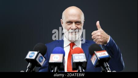 Politician giving a thumbs up during a press conference and smiling Stock Photo