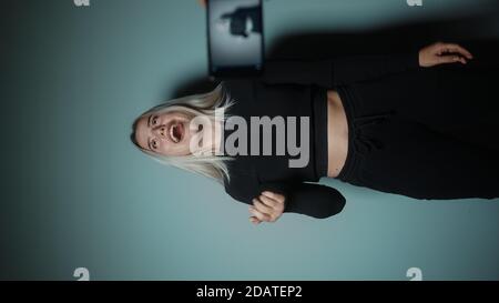 Blogger blonde woman making online new video blog, vlog, with her smartphone on studio background. Influencer speaking to smartphone during conference Stock Photo