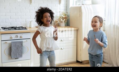 Overjoyed diverse little girls playing with kitchenware in kitchen together Stock Photo