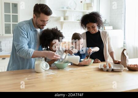 Happy diverse parents with kids cooking dough in modern kitchen Stock Photo