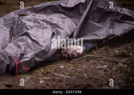 Dead man body In the woods. Caucasian man body covered with sheet . Dead man hand. Murder in the woods Stock Photo