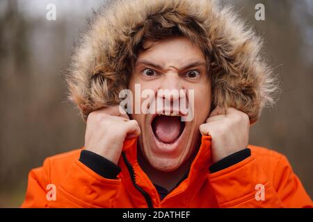 Portrait of young screaming man in hood. Close up of funny guy aping, standing in forest Stock Photo