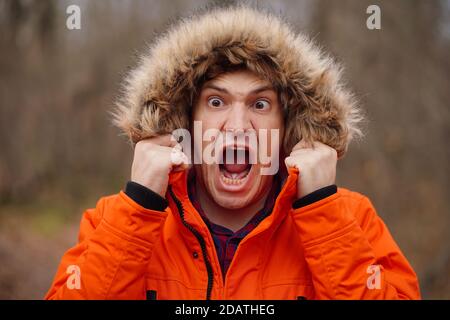 Portrait of young screaming man in hood. Close up of funny guy aping, standing in forest Stock Photo