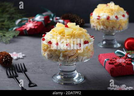 Festive salad with chicken, pineapple, cheese and eggs in portioned bowls on dark gray background. New Year still life. Stock Photo