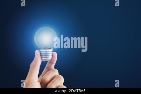 Hand holding glowing light bulb, on blue background Stock Photo