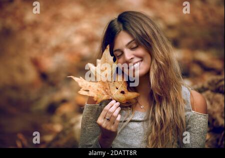 Portrait of a Beautiful Girl Enjoying  Autumn Forest. Holding in Hand Dry Maple Leaf. Happy Positive Face. Beauty of Fall Season Stock Photo