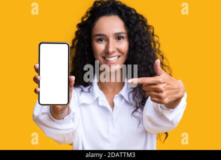 Mockup Image Of Brunette Woman Pointing At Smartphone With Blank White Screen Stock Photo