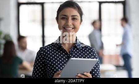 Smiling indian female manager standing in office holding digital tablet Stock Photo