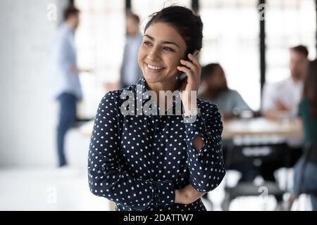 Positive indian lady consultant standing at workplace talking on phone Stock Photo