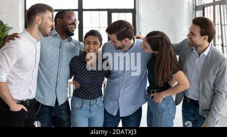 Excited overjoyed millennial multiethnic teammates hugging celebrating common achievement Stock Photo