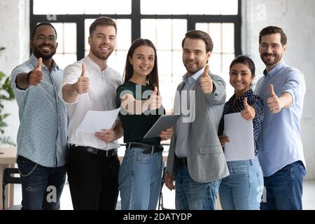Group of young multiethnic employees standing together raising thumbs up Stock Photo