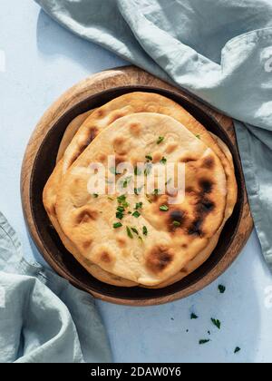 Stack of fesh naan breads in cast-iron pan on blue background with copy space. Top view of perfect naan flatbreads in black circle cast iron pan. Vertical. Stock Photo