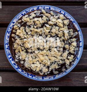 Cocoa and coconut cake covered with chocolate glaze and almond flakes, on wooden background Stock Photo