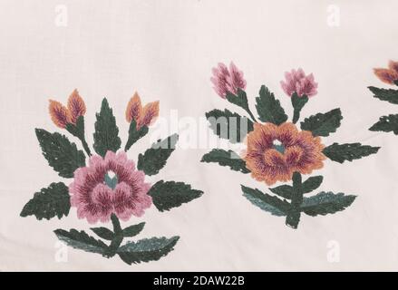 Crafts: beautiful red flowers and green leaves embroidery stitch. Embroidery on white cotton fabric. Stock Photo