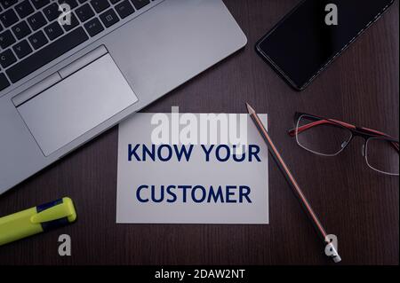 Top view of laptop, phone, glasses and pencil with card with inscription know your customer. Business concept. Stock Photo
