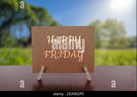 Happy Friday card on the table with sunny green forest background. Stock Photo