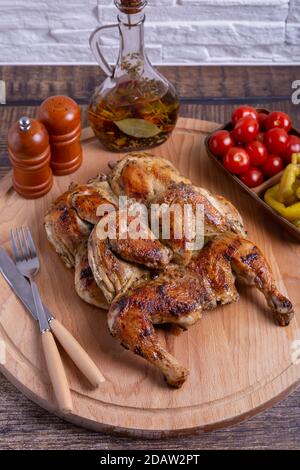 Tapaca (tabaca) chickens with cherry tomatoes and pepperoni on a wooden board. Traditional Georgian dish. Close-up. Stock Photo