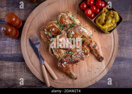Tapaca (tabaca) chickens with cherry tomatoes, pepperoni and garlic and cilantro on a wooden board. Traditional Georgian dish. Close-up. Stock Photo