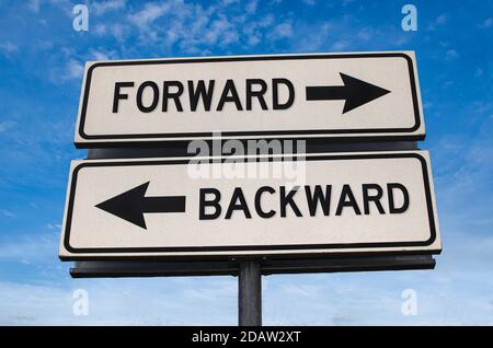 Forward vs backward. White two street signs with arrow on metal pole with word. Directional road. Crossroads Road Sign, Two Arrow. Blue sky background Stock Photo