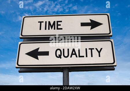 Time and quality white two arrows signs on metal pole. Directional road. Crossroads Road Sign, Two Arrows against blue sky background. Two way road si Stock Photo