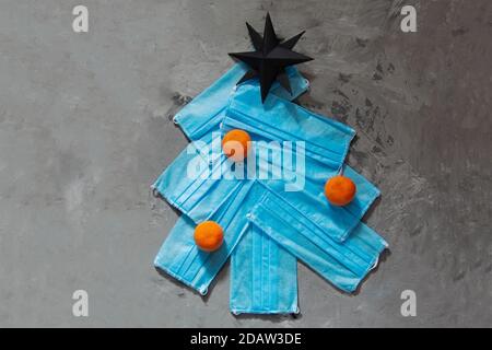 Christmas tree made from face masks with orange tangerine decor on grey concrete background. New year's eve 2021 in the context of the coronovirus pan Stock Photo