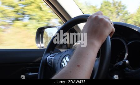 Closeup of young man hand holding steering wheel while speed driving Suzuki car. Blur view of autumn yellow trees outside auto windows. Odessa, Ukrain Stock Photo