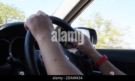 Closeup of young man hands holding steering wheel while speed driving a car. Blur view of autumn yellow trees outside the side window and windshield Stock Photo