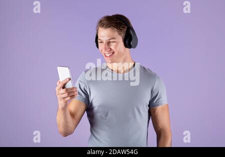 Young sporty guy with smartphone listening to music in headset on violet studio background Stock Photo