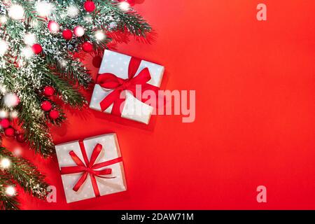 Xmas festive background with fir branches with snow, red berries, two DIY gift boxes tied with ribbons and bows on red. Stock Photo