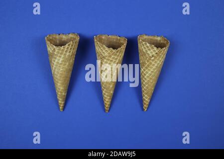 Close up of three isolated ice cream waffle cones on blue blank background (focus on upper part of cones) Stock Photo