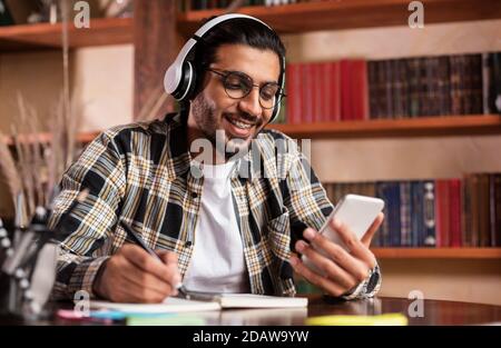 Happy Indian Student With Smartphone Learning Sitting In University Library Stock Photo