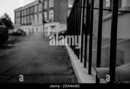 black and white monochrome image of steam appearing from a external building pipe at from a low level with background of blurred out row of Georgian h Stock Photo