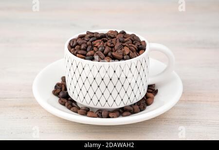 Coffee beans in a white ceramic Cup and saucer on a light background. Stock Photo