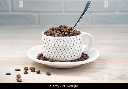 White coffee Cup full of coffee beans and a spoon on a light background. Stock Photo
