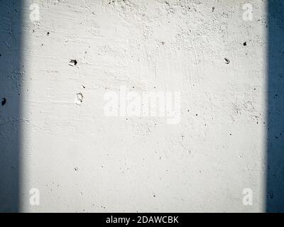 White concrete wall with irregularities is lit by sun and shadows on sides. Empty building surface, copy space. Stock Photo