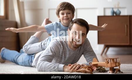 Funny portrait little boy pretending flying lying on father back Stock Photo