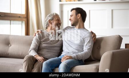 Happy mature father and adult son chatting, sitting on couch Stock Photo